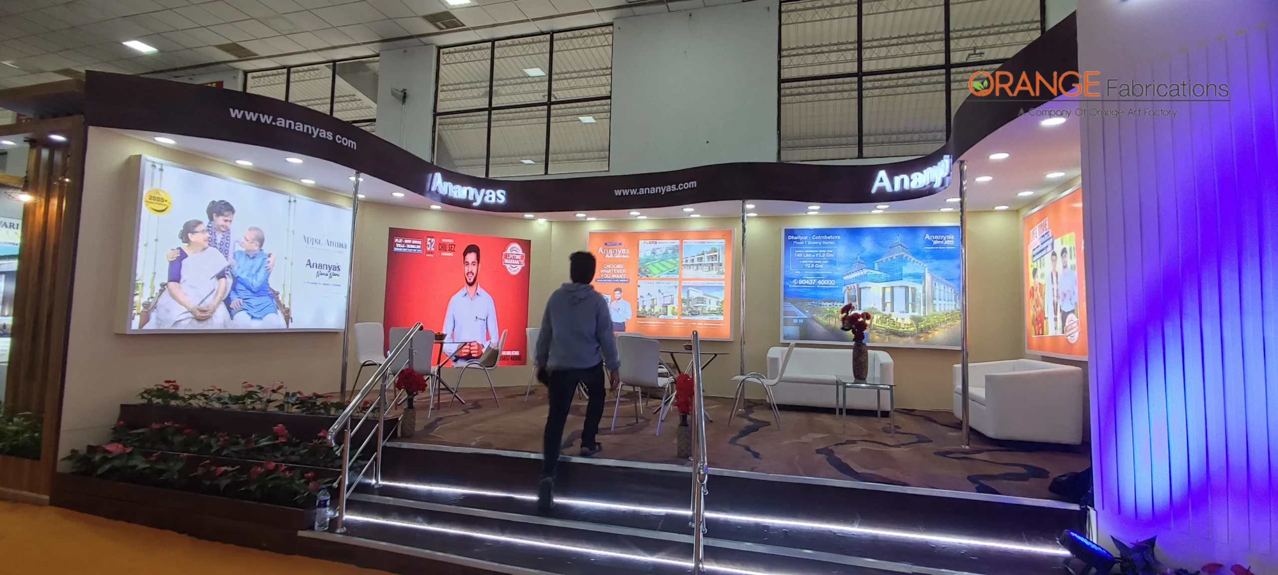 custom curved wooden exhibition stall with raised platform, LED step lighting, and backlit graphic displays fabricated for Ananyas at CREDAI FairPro, CODISSIA Coimbatore